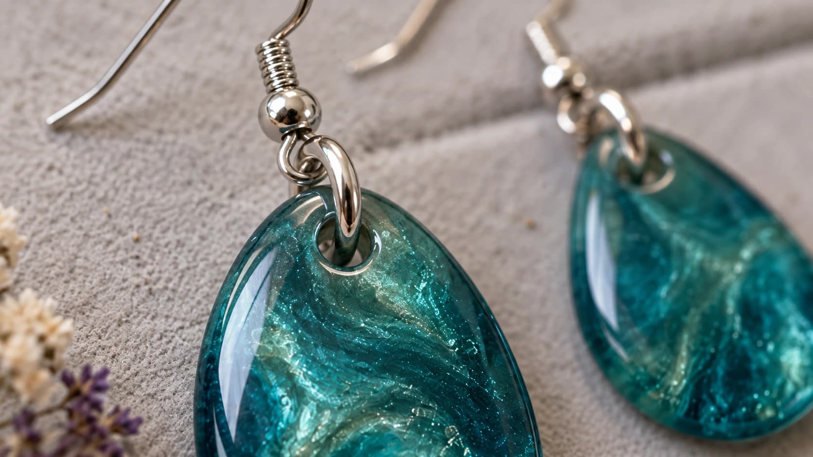 Close view of teal resin earrings with closed jump rings passing through their top holes and connecting to ear wires