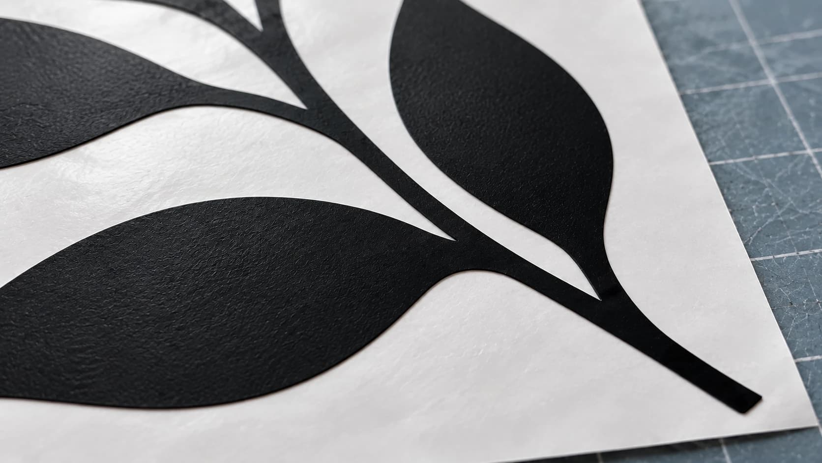 Close view of the same black leaf decal on white release paper and a blue-gray mat