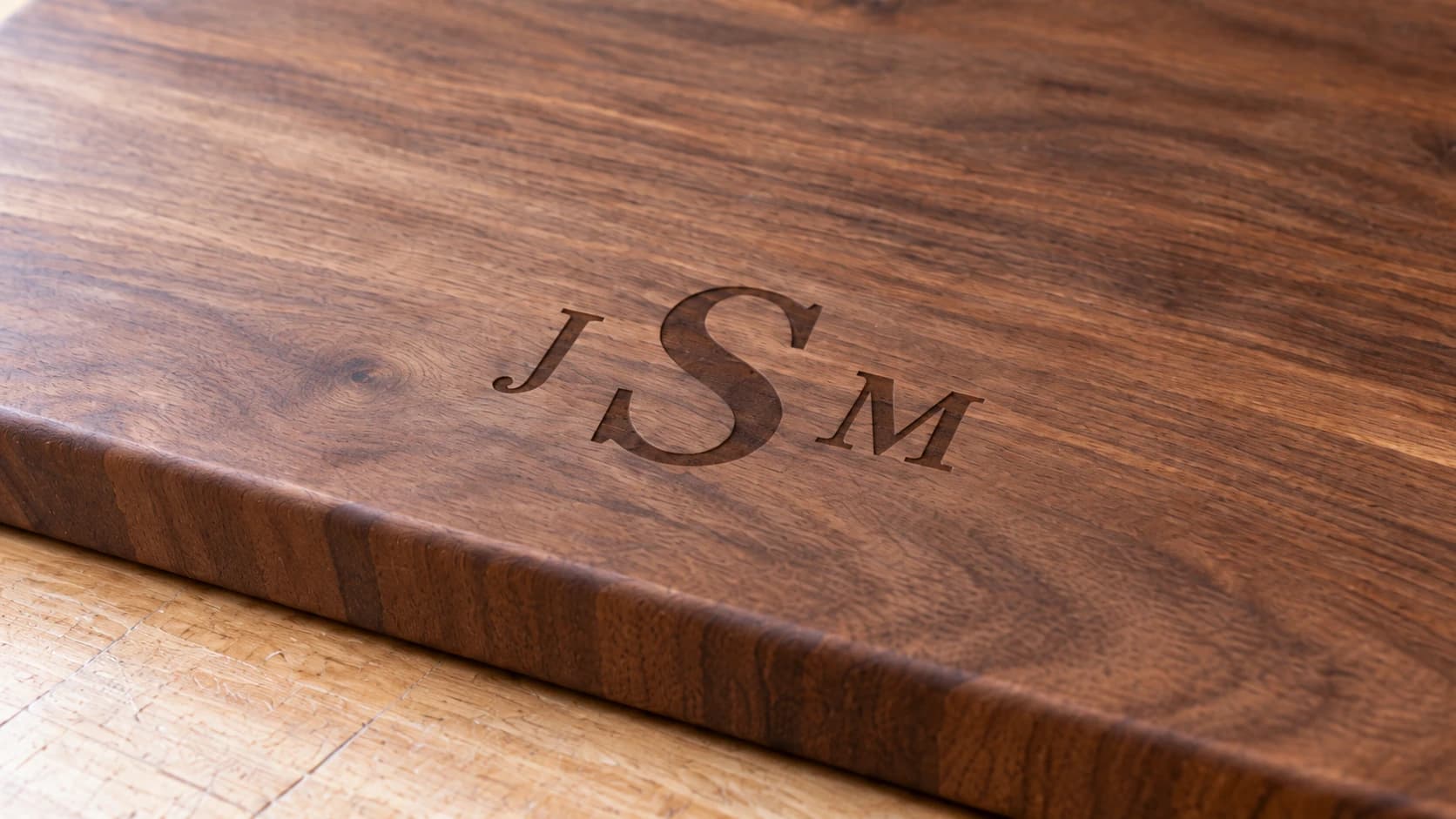 Close view of the same walnut board showing shallow brown J-S-M engraving and continuous wood grain