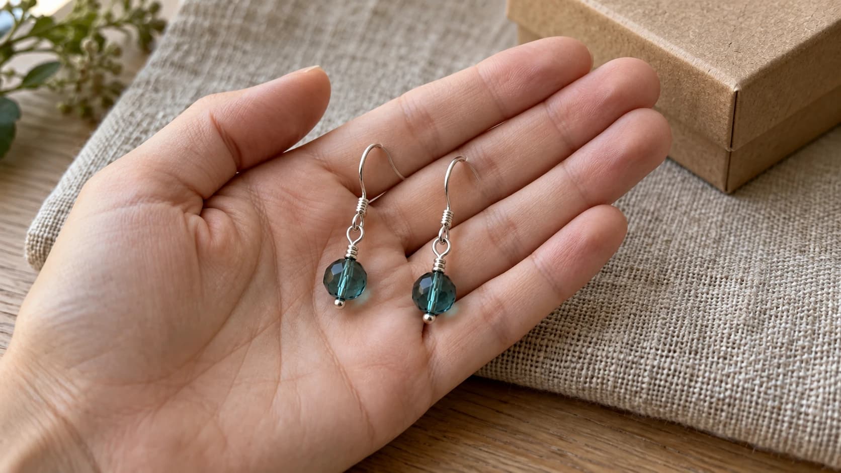 The matching teal bead earrings resting on an open palm above the same linen-covered table