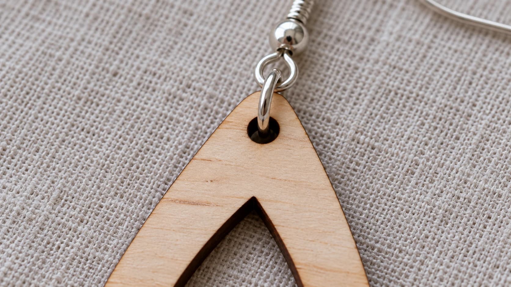 A silver jump ring passing through the actual hanging hole in a birch teardrop earring