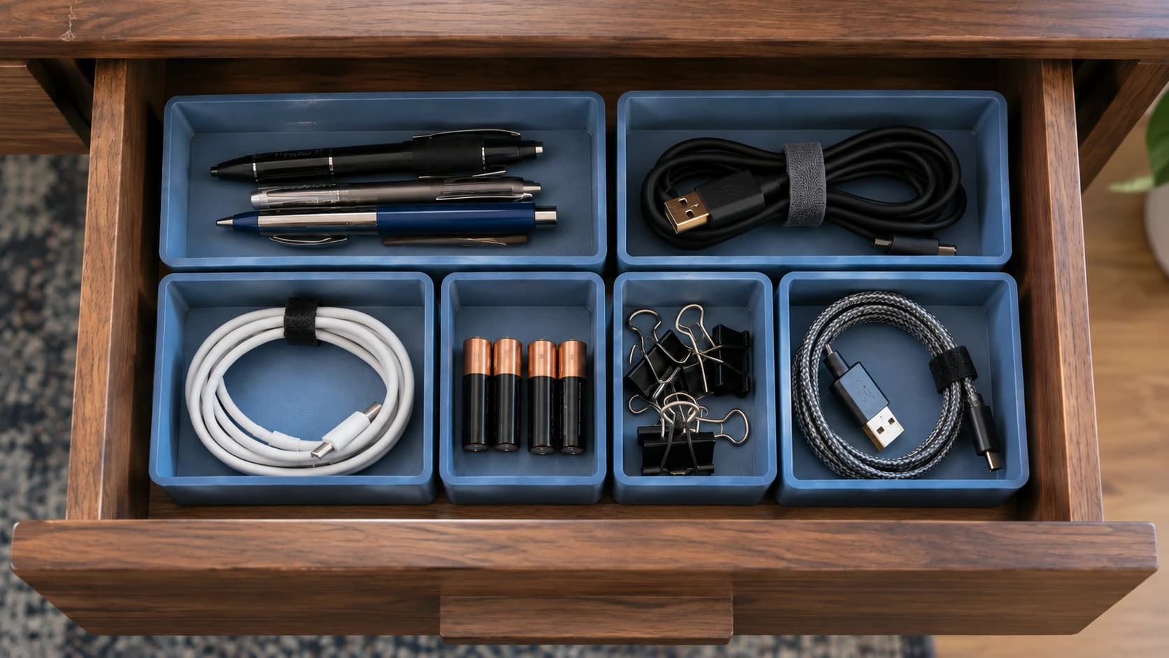 Overhead view of six blue printed bins fitted to the walnut drawer and holding sorted desk supplies